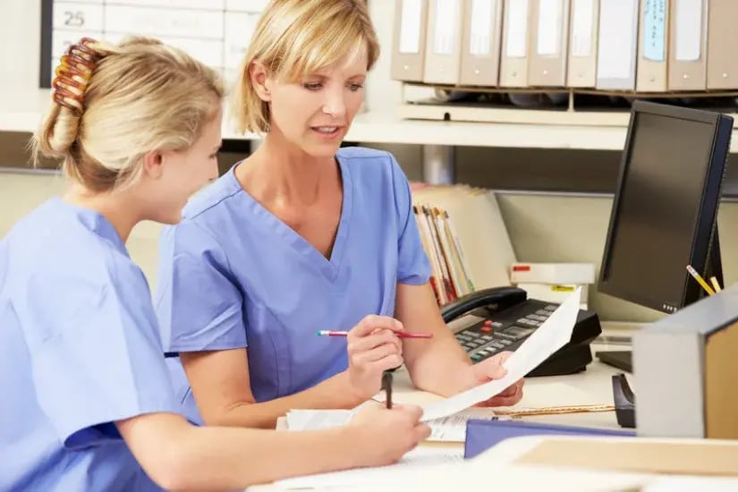 Zwei Pflegekräfte besprechen im Stationszimmer Unterlagen zur Dienstplanung – Symbolbild für Personalbedarf in der Pflege
